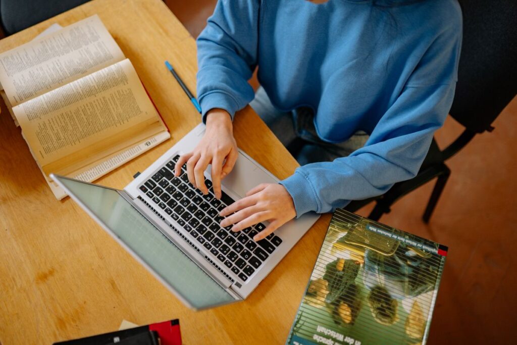 Student typing a ChatGPT prompt surrounded by open textbooks